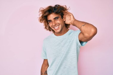 Gündelik kıyafetler giyen, ağzı kulaklarında gülümseyen genç İspanyol bir adam dedikoduları ve dedikoduları dinliyor. Sağırlık kavramı. 