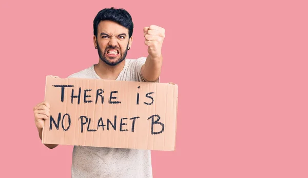 Young hispanic man holding there is no planet b banner annoyed and frustrated shouting with anger, yelling crazy with anger and hand raised