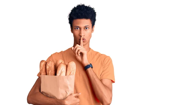 若いアフリカ系アメリカ人の男性がパンと紙の袋を保持し 唇に指で静かになるように求めている 沈黙と秘密の概念 — ストック写真