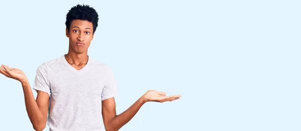 年轻的非洲裔美国人 身穿休闲的白色T恤 毫无头绪 满脸困惑 手臂和双手高举 怀疑概念 — 图库照片