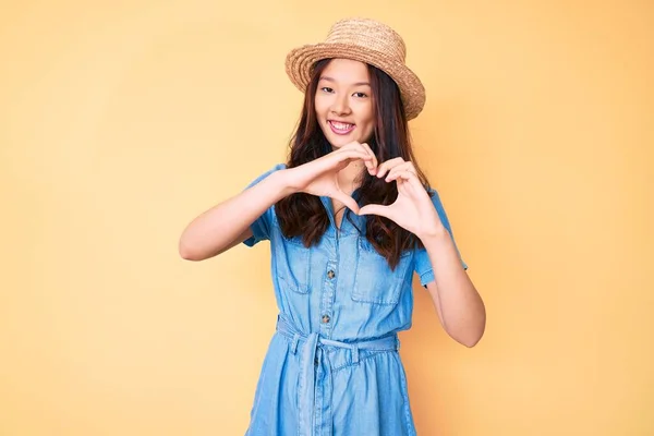 年轻美丽的中国姑娘戴着夏帽 带着爱的笑容用手做心形符号 浪漫的概念 — 图库照片