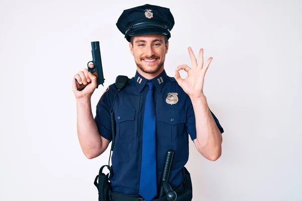 年轻的高加索人 身穿警服 拿着枪 手拿着手签 微笑着友好的手势 展示着优秀的标志 — 图库照片