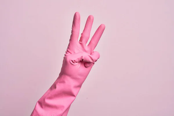 带着清洁手套的高加索年轻人的手在孤立的粉色背景上数着3个手指 — 图库照片