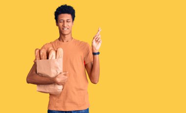 Afro-Amerikalı genç bir adam ekmek torbası tutuyor ve umut ve gözleri kapalı bir şekilde gülümsüyor. Şans ve batıl inançlar. 