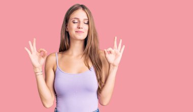 Kolsuz tişörtlü, sıradan giyinen genç, güzel sarışın kadın rahatla ve parmaklarıyla meditasyon hareketi yaparken gözleri kapalı gülümse. yoga konsepti. 