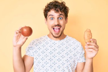 Kıvırcık saçlı, elma ve kruvasan tutan genç beyaz adam çılgınlığı kutluyor ve başarı için hayrete düşüyor.. 