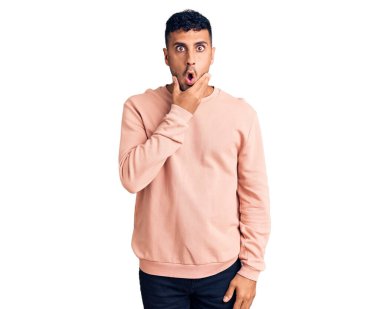 Gündelik kıyafetler giyen genç İspanyol adam, elleri çenesinde, inanamama, şaşkınlık ve şaşkınlık dolu bir ifade takınıyor. 