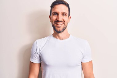 Yüzünde mutlu ve havalı bir gülümsemeyle izole edilmiş beyaz arka plan üzerinde duran sıradan tişört giyen genç yakışıklı bir adam. Şanslı kişi..