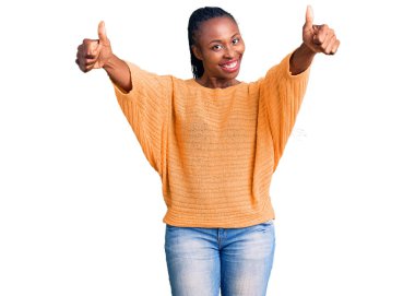 Genç Afro-Amerikalı kadın, günlük giysiler giyip, olumlu jestler yapıyor, gülümsüyor ve başarı için seviniyor. kazanan jest. 