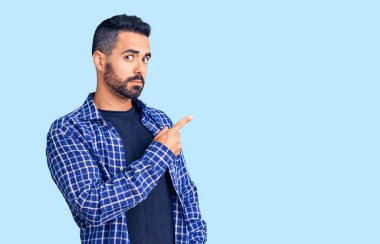 Gündelik giysiler giymiş genç İspanyol bir adam el ile işaret ediyor. Ciddi ve sakin bir yüz ifadesi sergiliyor. 