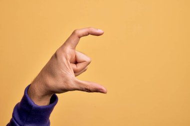 İzole edilmiş sarı arka plan üzerinde parmaklarını gösteren beyaz bir adamın eli. Görünmez bir şeyi alıp, parmaklarıyla uzayı gösteren bir nesneyi tutuyor.