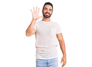 Gündelik kıyafetler giyen genç İspanyol adam beş numarayı gösterip işaret ederken kendinden emin ve mutlu bir şekilde gülümsüyor.. 