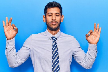 İş kıyafetleri giyen genç latin adam rahatla ve gözleri kapalı gülümse parmaklarıyla meditasyon hareketi yapıyor. yoga konsepti. 