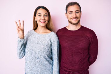 Güzel bir çift gündelik giysiler giyer ve üç numarayı göstererek gülümserken kendinden emin ve mutlu görünürler.. 