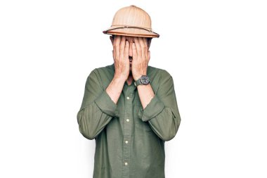 Tatilde olan orta yaşlı bir turist, izole edilmiş beyaz arka plan üzerinde gezen bir kaşif şapkası takıyor. Unuttum, kötü hafıza konsepti.