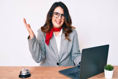 Genç, güzel esmer kadın otel resepsiyonunda dizüstü bilgisayar kullanarak zaferi kutluyor mutlu bir gülümsemeyle ve ellerini kaldırarak kazanan bir ifadeyle. 