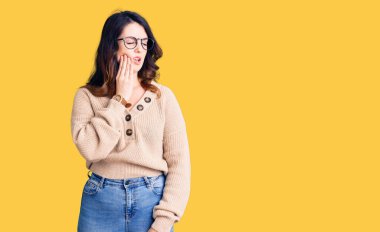 Güzel, genç, esmer, günlük kıyafetler giyen ve gözlüklü bir kadın diş ağrısı ya da diş hastalığından dolayı ağızlarına acı dolu bir ifadeyle dokunuyor. dişçi 