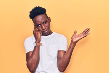 Genç Afro-Amerikalı bir adam günlük giysiler giymiş. Kafası karışmış ve avuç içi açık bir şekilde fotokopi alanı göstermekten rahatsız olmuş ve alnını işaret ediyor. Bunu bir düşün.. 