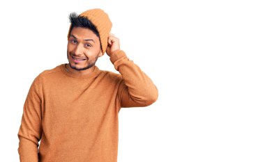 Kış süveteri ve yün şapka giyen yakışıklı Latin Amerikalı genç adam soru sorup kafasını karıştırıyor. Şüpheyle kararsız, kafa kafaya düşünerek. Düşünceli kavram. 