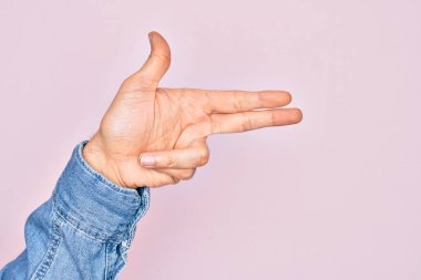 İzole edilmiş pembe arka planda parmaklarını gösteren beyaz bir gencin eli. Ateşli tabancayı parmaklarıyla işaret ediyor.