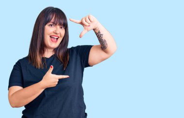 Gündelik kıyafetler giyen, gülümseyen, elleri ve parmakları mutlu yüzlü, çerçeveli genç bir kadın. yaratıcılık ve fotoğrafçılık kavramı. 