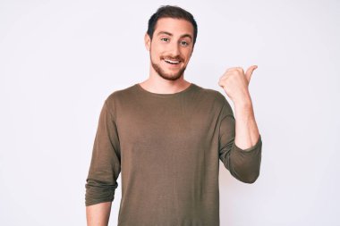Genç, yakışıklı, sıradan kıyafetler giyen, gülen yüzlü, gülümseyen ve baş parmağıyla yan tarafı gösteren bir adam.. 