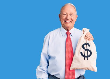 Üst düzey yakışıklı, gri saçlı şık kıyafetler giyen, para çantası tutan, pozitif ve mutlu görünen, kendine güvenen, gülümseyen, dişlerini gösteren bir adam. 