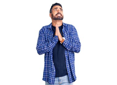 Gündelik giysiler giyen genç İspanyol adam elleri bağlı yalvarıyor ve dua ediyor. Yüzünde umut ifadesi var. Çok duygusal ve endişeli. Yalvarıyor. 