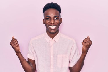Genç Afrikalı Amerikalı sıradan kıyafetler giymiş gururla bağıran, zaferi kutlayan ve kollarını kaldırarak heyecanlanan genç bir adam. 