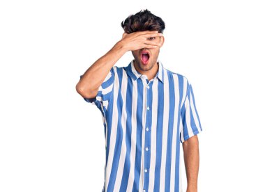 Gündelik kıyafetler giyen genç İspanyol adam şok içinde yüzünü ve gözlerini kapayarak utanmış ifadesiyle parmaklarından bakıyor.. 