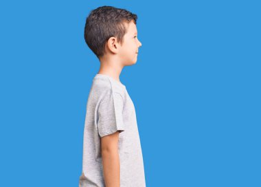 Hoş sarışın çocuk günlük giysiler giyiyor. Tarafını arıyor, rahat poz veriyor. Kendine güvenen bir gülümsemesi var.. 