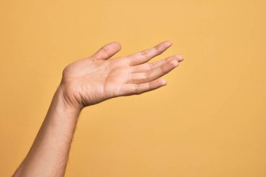 İzole edilmiş sarı arka plan üzerinde parmaklarını gösteren beyaz bir genç adam. Avuç içi açık bir şekilde destek ve yardım için uzanıyor.
