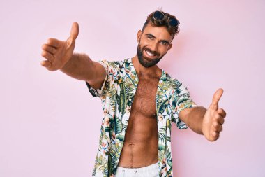 Yaz kıyafetleri giymiş genç İspanyol bir adam baş parmağını kaldırmış, ağzı açık gülümsüyor. 