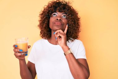 Genç Afrikalı Amerikalı bir kadın bir bardak portakal suyu içiyor ciddi bir yüz ifadesi var eli çenesinde soruyu düşünüyor, kafa karıştırıcı bir fikir. 