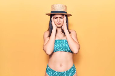 Bikini ve yaz şapkası takan genç ve güzel bir kız baş ağrısı yüzünden çaresiz ve stresli çünkü acı ve migren. Eller başının üstünde.. 