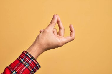 İzole edilmiş sarı arka planda parmaklarını gösteren beyaz bir gencin eli. Başarı için parmaklarını şıklatıyor, kolay ve eliyle sembolü tıklatıyor.