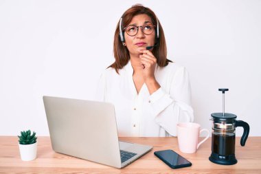 Orta yaşlı esmer, ofiste çalışan, operatör kulaklığı takan, parmakları çenesinde şüpheye odaklanmış ve kafasını kaldırıp, 