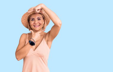 Sarışın, yaz şapkası takan, gülümseyen, elleri ve parmakları olan mutlu yüzlü genç bir kadın. yaratıcılık ve fotoğrafçılık kavramı. 