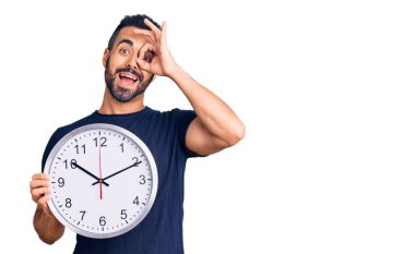 Büyük bir saat tutan İspanyol genç adam gülümsüyor. Mutluluktan gülümsüyor. 