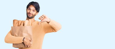 Yakışıklı İspanyol bir adam elinde kızgın suratlı bir ekmek torbası, olumsuz işaretler baş parmakları aşağıda, reddedilme konsepti. 