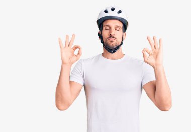 Bisiklet kaskı takan yakışıklı genç adam rahatla ve gözleri kapalı gülümse parmaklarıyla meditasyon hareketi yapıyor. yoga konsepti. 