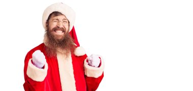 Uzun sakallı, yakışıklı, Noel Baba kostümü giyen, kolları havada ve gözleri kapalı zaferi kutlayan yakışıklı genç adam. Kazanan konsept. 