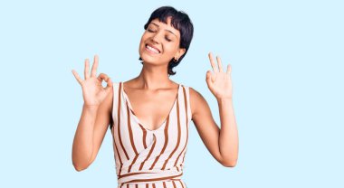 Kısa saçlı, kısa saçlı, yaz kıyafeti giyen, gözleri kapalı gülümseyen ve parmaklarıyla meditasyon yapan genç esmer kadın. yoga konsepti. 