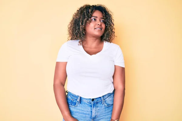 若いアフリカ系アメリカ人のプラスサイズの女性の顔に笑顔で横に離れて見てカジュアルな白いTシャツを着て 自然な表情 自信を持って — ストック写真