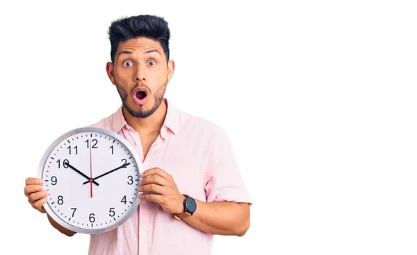 大きな時計を持っているハンサムなラテン系アメリカ人の若い男は怖がって 驚きのために口を開けて驚いて 不信の顔 — ストック写真