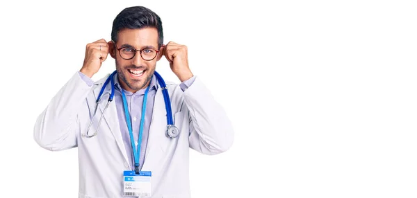 Young Hispanic Man Wearing Doctor Uniform Stethoscope Smiling Pulling Ears — Stock Photo, Image