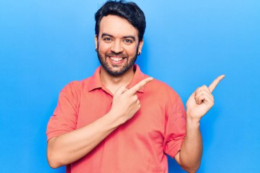 Gündelik kıyafetler giyen genç İspanyol adam gülümseyip kameraya bakıyor ve iki eliyle ve parmaklarıyla kenarı işaret ediyor.. 