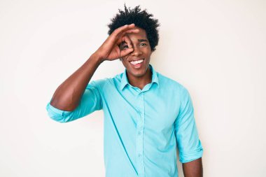 Afro saçlı yakışıklı bir Amerikalı. Günlük kıyafetler giyiyor. El hareketleriyle gülümsüyor. Gözleri, mutlu yüzüyle parmaklarının arasından bakıyor.. 