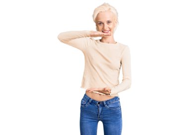 Genç sarışın kadın, sıradan kıyafetler giyiyor. Elleriyle işaret ediyor. Büyük ve büyük beden işareti, ölçü sembolü. Kameraya bakıp gülümsüyor. ölçüm kavramı. 