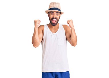 Gündelik yaz şapkası takan İspanyol genç adam şaşkınlık ve şaşkınlık içinde kollarını kaldırarak ve gözlerini açarak başarıyı kutluyor. Kazanan konsept. 